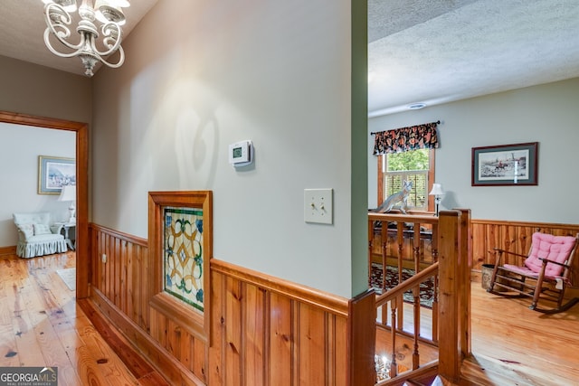 hallway with an upstairs landing, hardwood / wood-style floors, wainscoting, a chandelier, and a textured ceiling