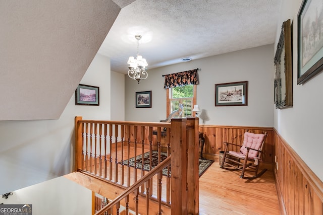 stairway featuring wood finished floors, a textured ceiling, a chandelier, wainscoting, and wood walls