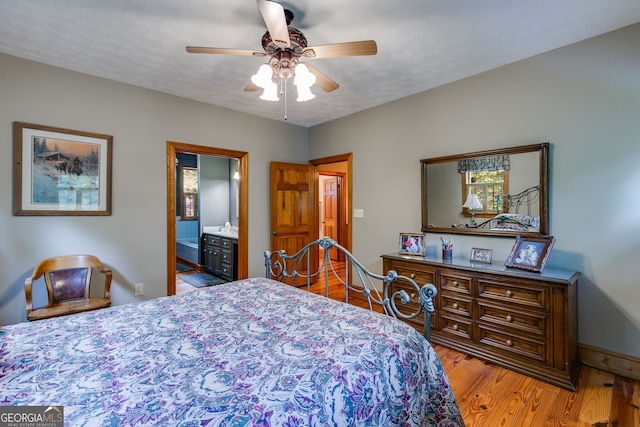 bedroom featuring wood finished floors, baseboards, ensuite bathroom, and a ceiling fan