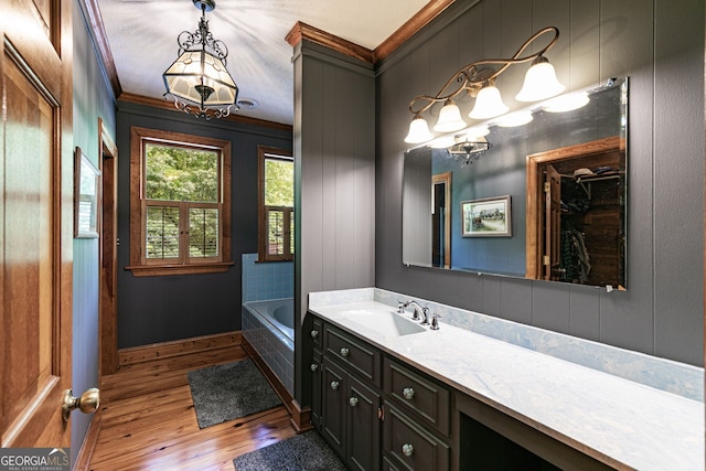 bathroom with wood finished floors, a chandelier, ornamental molding, vanity, and a garden tub