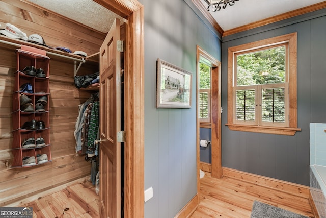 hallway featuring wood finished floors, baseboards, crown molding, and wood walls