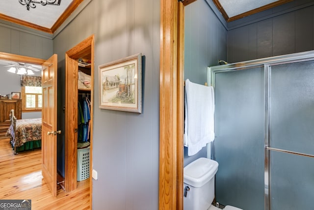 bathroom featuring crown molding, wood finished floors, a stall shower, toilet, and a ceiling fan