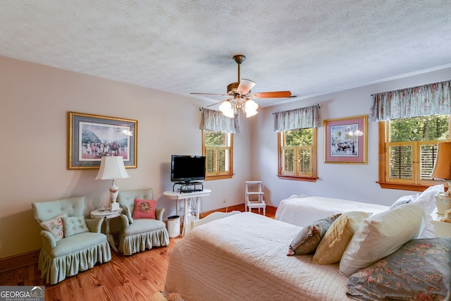 bedroom featuring multiple windows, wood finished floors, a textured ceiling, and baseboards