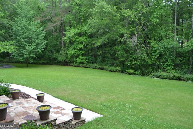 view of grassy yard with a view of trees and a patio area