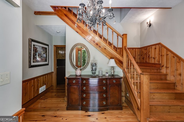 stairs featuring a chandelier, hardwood / wood-style floors, wainscoting, and wooden walls