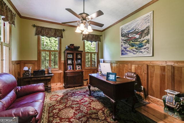 office area featuring wood finished floors, a wainscoted wall, ornamental molding, and a ceiling fan