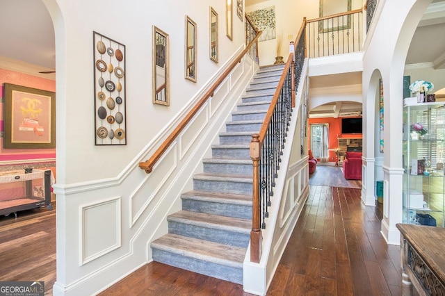stairway featuring hardwood / wood-style flooring, a fireplace, a decorative wall, arched walkways, and crown molding