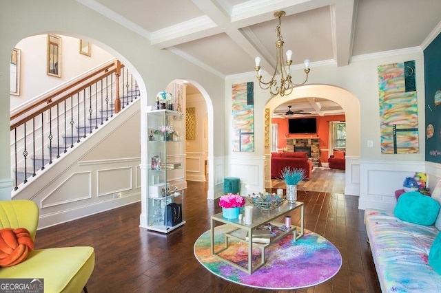 living room featuring beam ceiling, wood-type flooring, arched walkways, a decorative wall, and wainscoting
