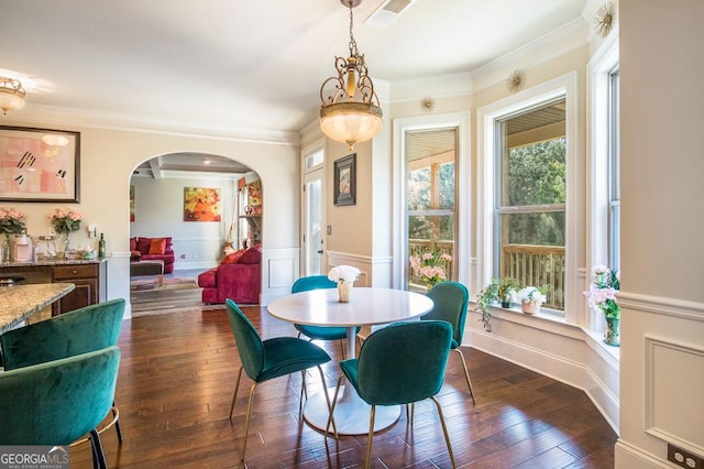 dining room featuring arched walkways, a wainscoted wall, dark wood finished floors, ornamental molding, and a decorative wall