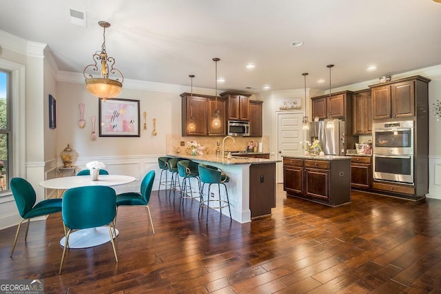 kitchen with appliances with stainless steel finishes, a peninsula, crown molding, light stone countertops, and a breakfast bar area