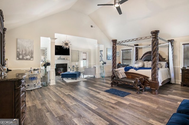 bedroom with high vaulted ceiling, dark wood-type flooring, a glass covered fireplace, and a ceiling fan