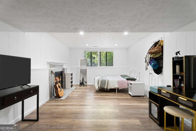 bedroom featuring wood finished floors, a textured ceiling, recessed lighting, a tile fireplace, and baseboards