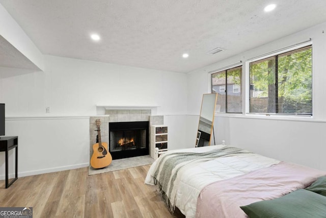 bedroom featuring wood finished floors, recessed lighting, a textured ceiling, and a tiled fireplace