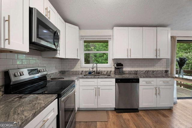 kitchen featuring appliances with stainless steel finishes, a sink, light wood-type flooring, white cabinets, and a textured ceiling