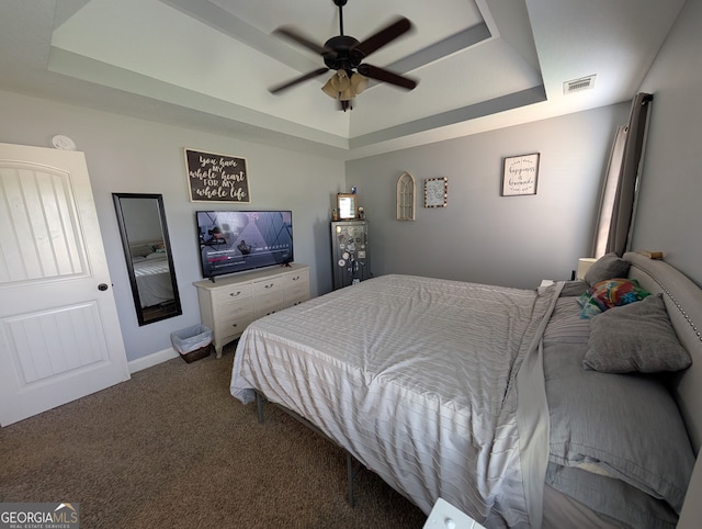 bedroom featuring a raised ceiling, dark carpet, a ceiling fan, and baseboards