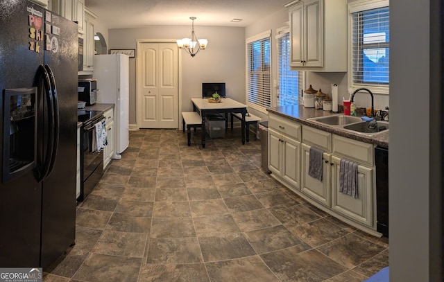 kitchen with black appliances, a sink, dark countertops, a chandelier, and stone finish flooring