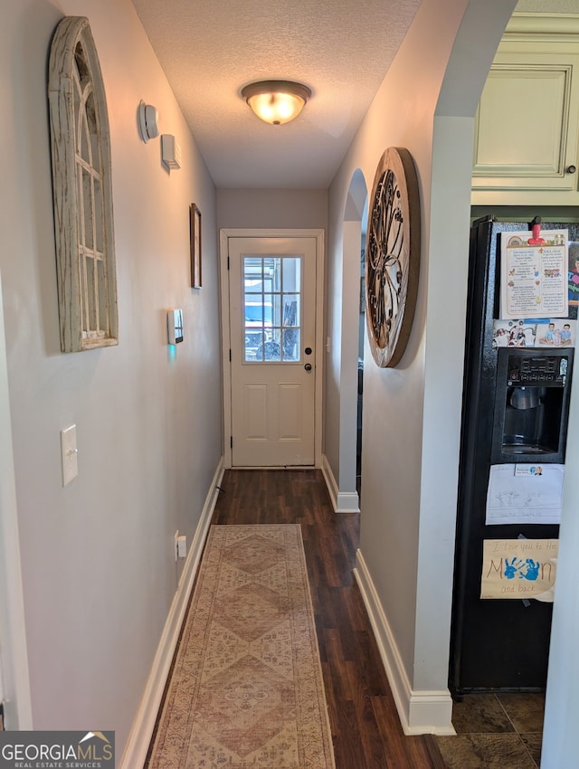 doorway to outside featuring baseboards, a textured ceiling, and dark wood-style floors