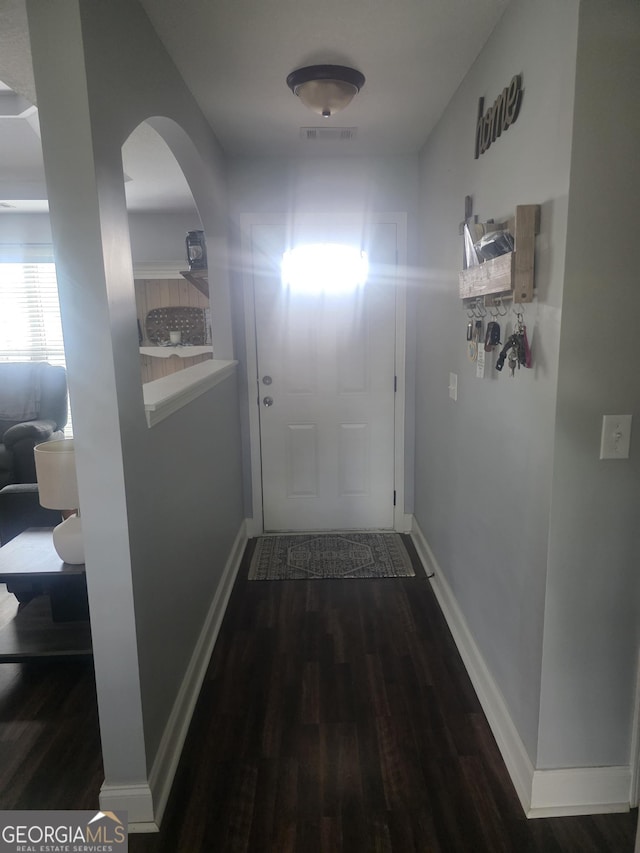 corridor with wood finished floors, arched walkways, and baseboards