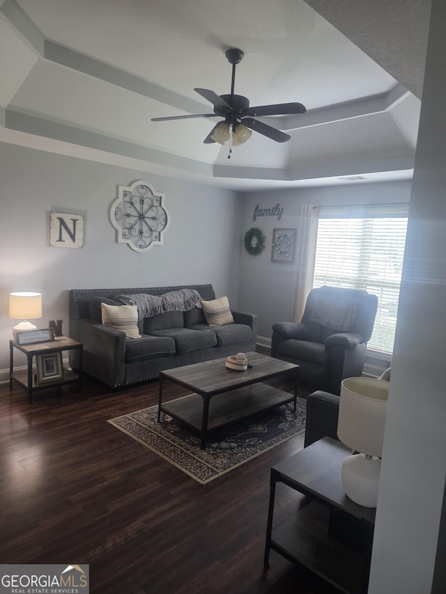 living area with wood finished floors, ceiling fan, a raised ceiling, and baseboards
