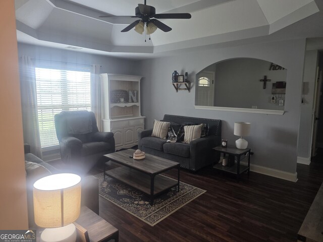 living area with a tray ceiling, ceiling fan, wood finished floors, baseboards, and arched walkways