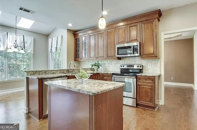 232 Spalding Gates Dr, Atlanta, GA 30328 - kitchen with stainless steel appliances, a peninsula, brown cabinets, light stone counters, and recessed lighting