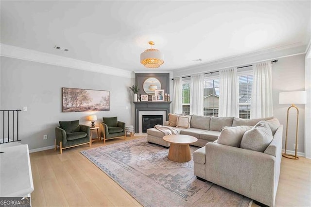 living area with crown molding, light wood-style flooring, baseboards, and a glass covered fireplace