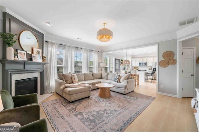 living room with crown molding, a glass covered fireplace, light wood-type flooring, and baseboards