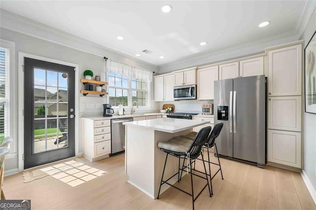 kitchen with appliances with stainless steel finishes, a sink, crown molding, a kitchen breakfast bar, and light countertops