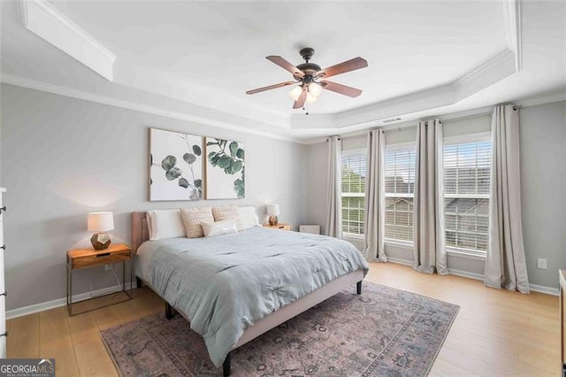 bedroom with a tray ceiling, light wood-style flooring, ornamental molding, baseboards, and ceiling fan