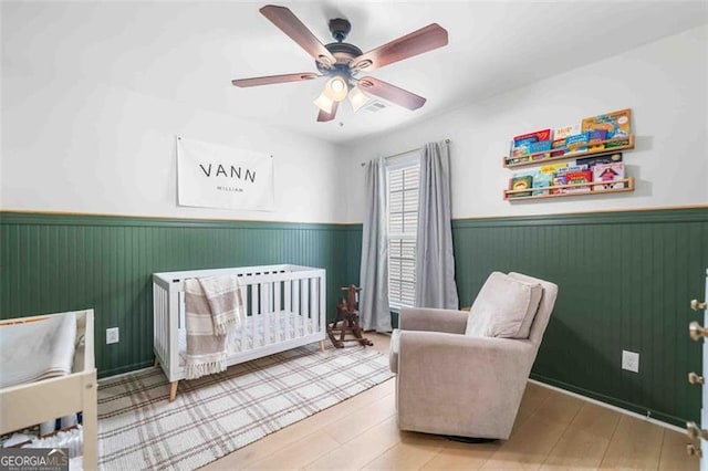bedroom with wainscoting, a crib, and a ceiling fan