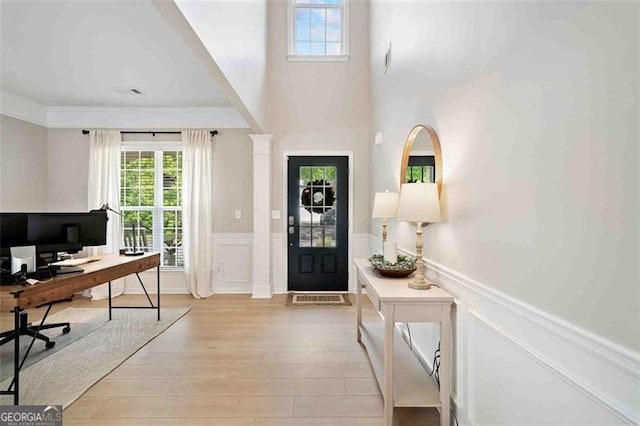 foyer with healthy amount of natural light, wainscoting, light wood-style floors, and a decorative wall