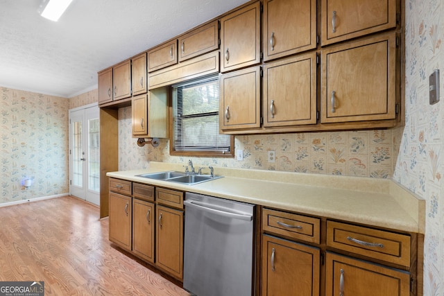 kitchen featuring stainless steel dishwasher, wallpapered walls, light wood-style floors, a sink, and light countertops