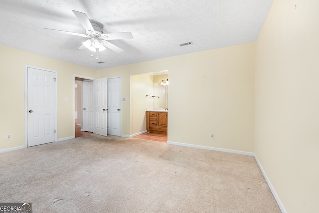 unfurnished bedroom with light colored carpet, baseboards, ensuite bathroom, a textured ceiling, and a ceiling fan