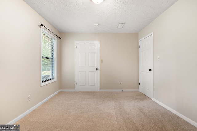 spare room featuring light carpet, a textured ceiling, and baseboards