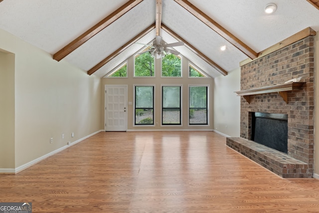unfurnished living room with light wood-style flooring, ceiling fan, beam ceiling, a brick fireplace, and baseboards