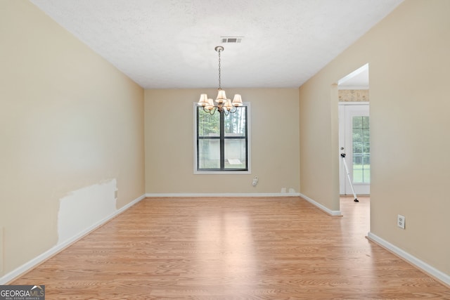 unfurnished room featuring light wood finished floors, a chandelier, healthy amount of natural light, baseboards, and a textured ceiling
