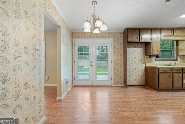 kitchen with light wood-style flooring, a sink, a chandelier, french doors, and wallpapered walls