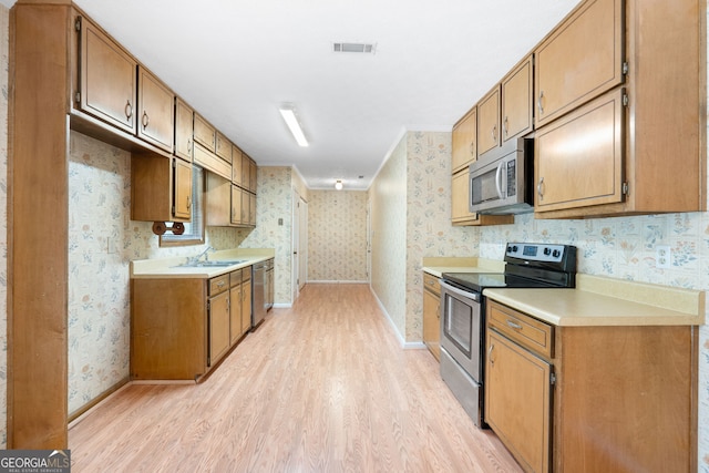 kitchen featuring appliances with stainless steel finishes, wallpapered walls, light wood-style floors, a sink, and baseboards