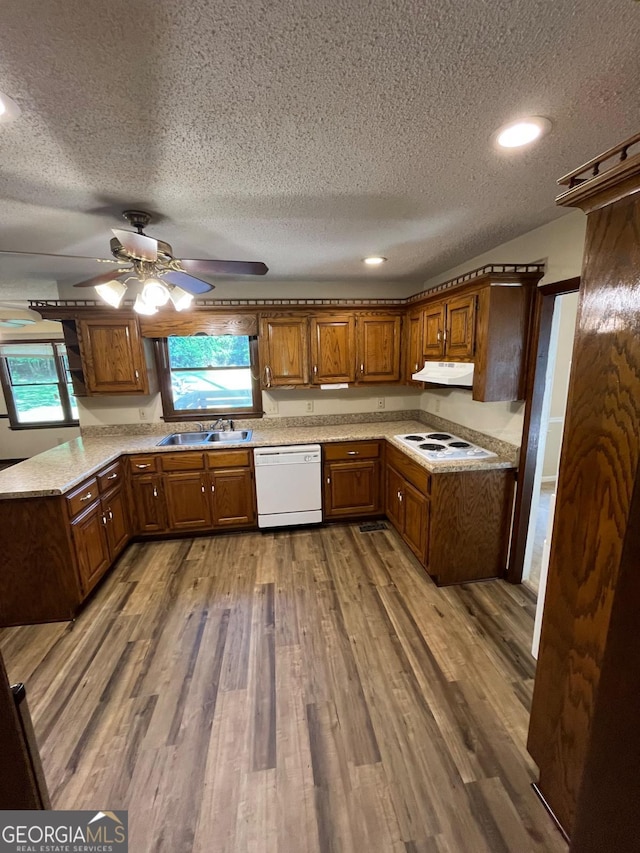 kitchen featuring white appliances, under cabinet range hood, a textured ceiling, light countertops, and a sink