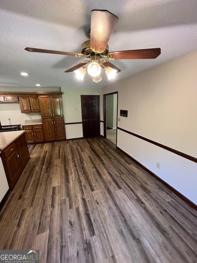 unfurnished dining area with a ceiling fan, dark wood-style flooring, baseboards, and a textured ceiling