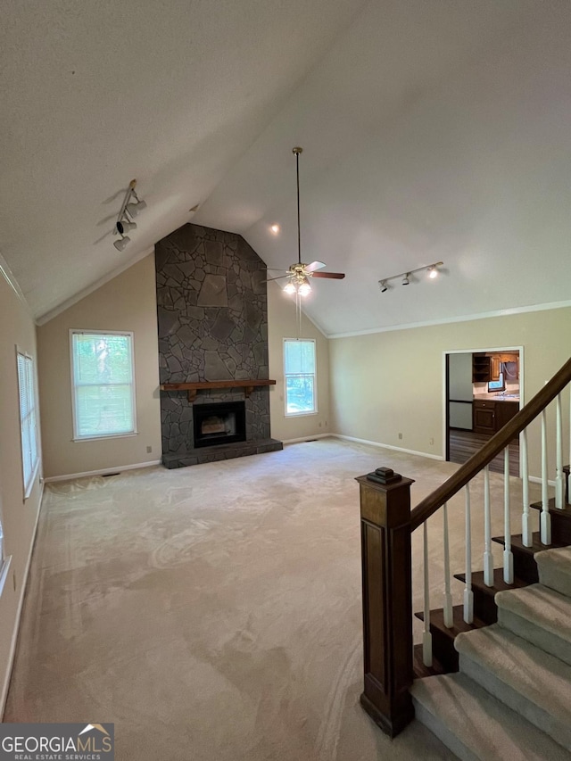 unfurnished living room featuring rail lighting, lofted ceiling, baseboards, a stone fireplace, and a ceiling fan