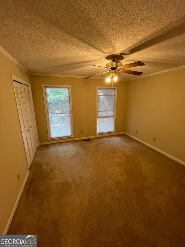 carpeted empty room with a textured ceiling, ornamental molding, baseboards, and a ceiling fan
