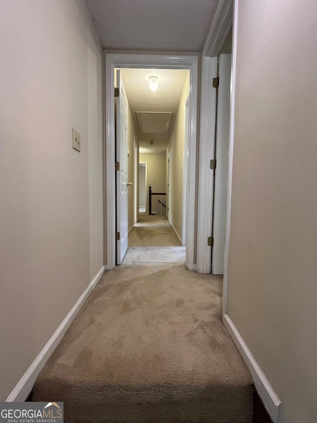 corridor featuring light carpet, attic access, a textured ceiling, and baseboards