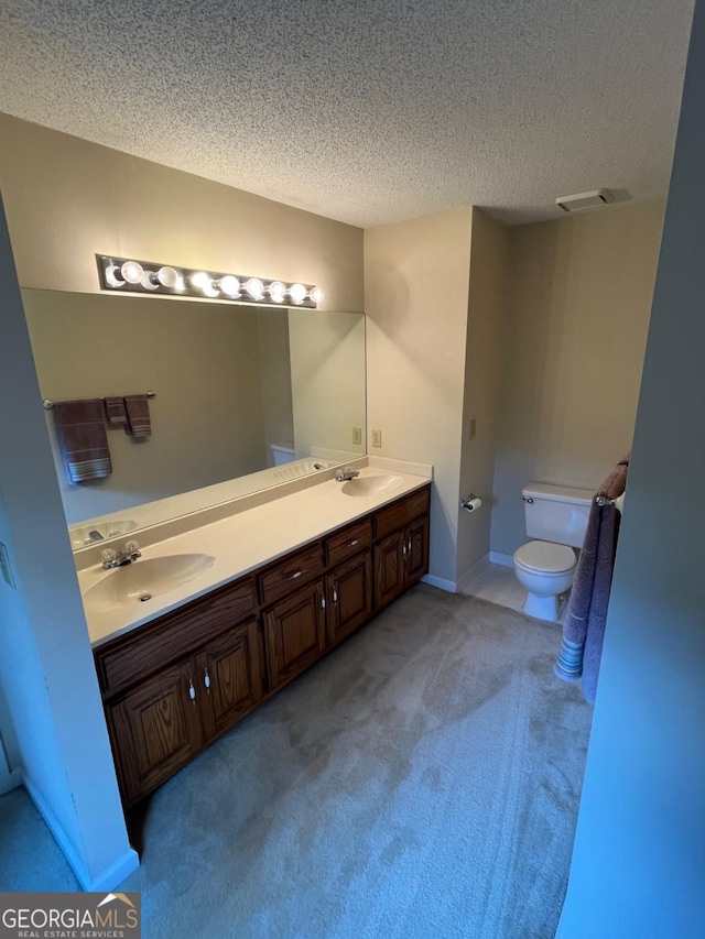 bathroom with toilet, a textured ceiling, and double vanity