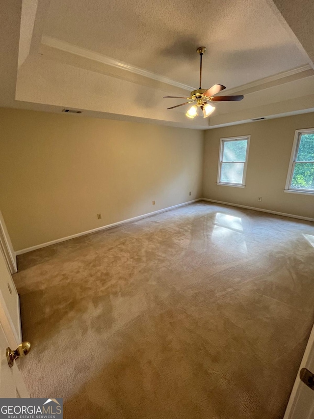 carpeted spare room featuring a raised ceiling, ceiling fan, a textured ceiling, and baseboards