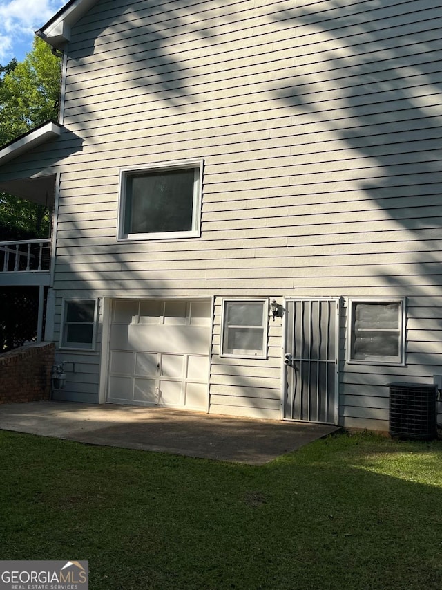rear view of house with central AC unit, an attached garage, and a yard