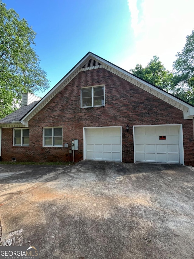view of side of property with brick siding, driveway, a garage, and a chimney