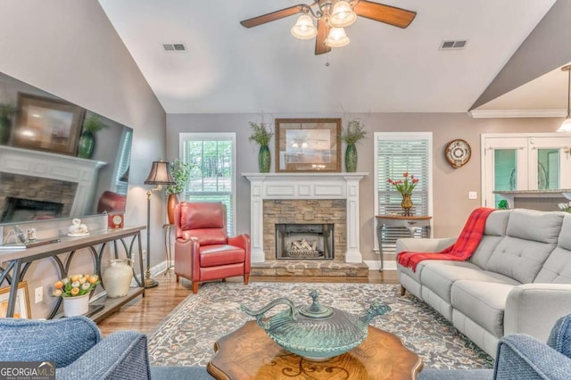 living room featuring a stone fireplace, lofted ceiling, a ceiling fan, wood finished floors, and baseboards
