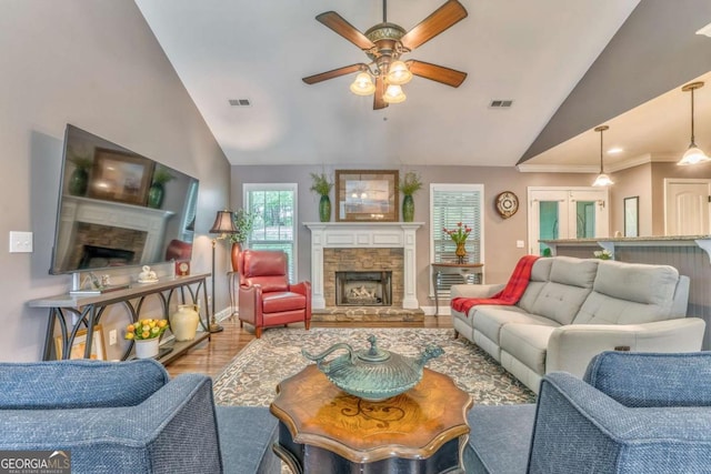 living area featuring a stone fireplace, ceiling fan, wood finished floors, high vaulted ceiling, and baseboards