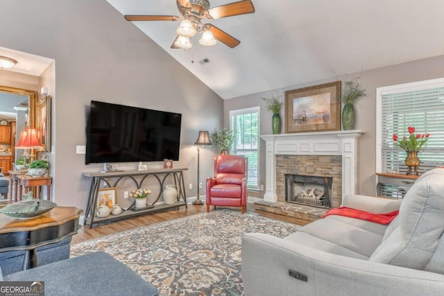 living room with a ceiling fan, wood finished floors, high vaulted ceiling, a stone fireplace, and baseboards